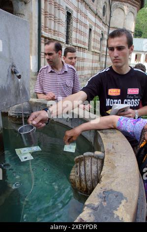 Besucher platzieren Münzen und Scheine in einem geheiligten Trinkbrunnen vor dem Kloster Cozia, Călimănești, Rumänien Stockfoto