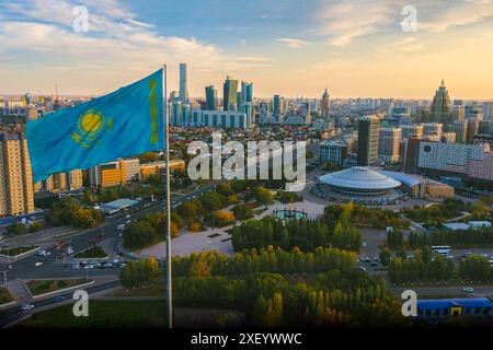 Die kasachische Flagge über der Stadt Astana mit Panoramablick auf die Innenstadt, den Zirkus der Hauptstadt, den grünen Park und die Geschäftsgebäude. Stockfoto