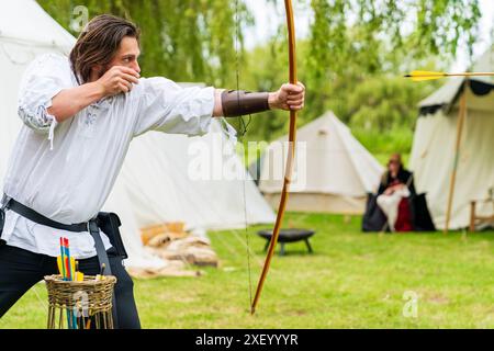 Nahaufnahme eines Mannes in mittelalterlichen Kostümen, der mit Pfeil und Bogen zielt und bei einer Nachstellung seinen Pfeil abfeuert. Stockfoto