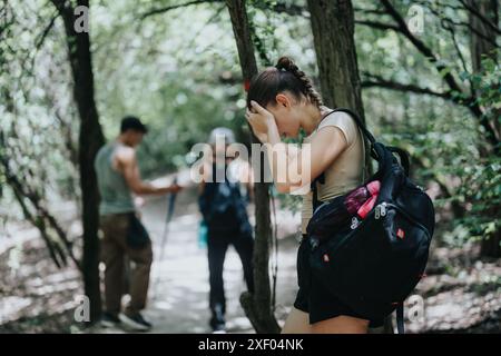 Junge Frau fühlt sich gestresst während einer Wanderung mit Freunden in einem dichten Wald Stockfoto