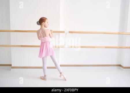 Ein junges Ballettmädchen beim Studiounterricht. Trainingsleistung. Stretching-Übungshaltung. Ballerina-Praxis-Balance-Technik. Klassische Eleganz Fitness. Tanzkostüm. Pinkfarbenes Kleid, Rock Stockfoto