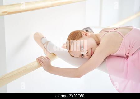 Ein junges Ballettmädchen beim Studiounterricht. Trainingsleistung. Stretching-Übungshaltung. Ballerina-Praxis-Balance-Technik. Klassische Eleganz. Tanzkostüm. Nahaufnahme, Garn. Pinkfarbenes Kleid, Rock Stockfoto