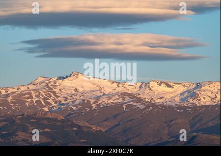 Riesige Lentikularwolken über den schneebedeckten Gipfeln der Sierra Nevada in Granada (Spanien) bei Sonnenuntergang Stockfoto
