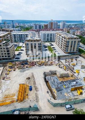 Eine Drohne fliegt durch die Baugrube eines neuen Wohnkomplexes mitten in der Stadt und erfasst die geschäftige Aktivität und die Umgebung Stockfoto