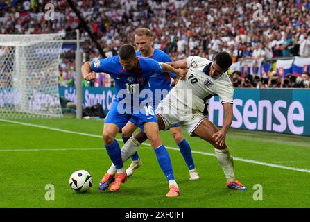 Der Engländer Jude Bellingham (rechts) kämpft um den Ball mit David Hancko (links) und Ondrej Duda (Mitte, hinten) um den Ball während der UEFA Euro 2024, im Achtelfinale in der Arena AufSchalke in Gelsenkirchen. Bilddatum: Sonntag, 30. Juni 2024. Stockfoto