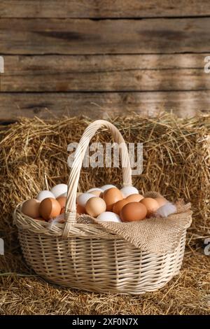 Frische Hühnereier im Korb auf getrocknetem Strohballen Stockfoto