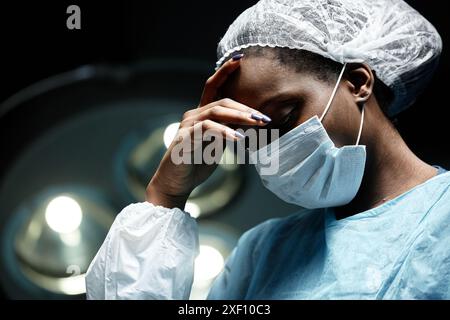 Dramatisches Porträt der jungen Afroamerikanerin als müde Chirurgin im OP im schwachen Kopierraum Stockfoto