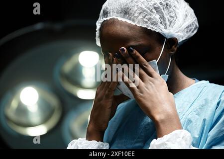 Dramatisches Porträt der jungen Schwarzen Frau als müde Chirurgin, die im Kopierraum des OP die Augen reibt Stockfoto