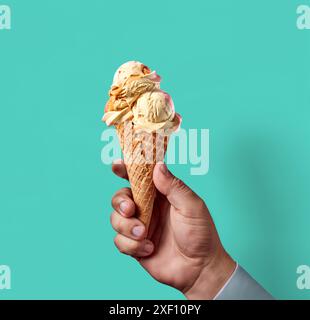 Köstliches Vanilleeis, gehalten von Menschenhand, blaue Hintergrundschablone Stockfoto