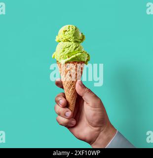 Köstliches Pistazieneis, gehalten von Menschenhand, blaue Hintergrundschablone Stockfoto