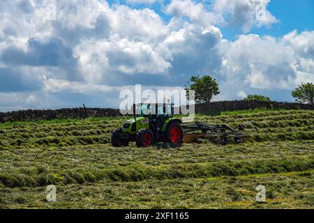 Grüner Traktor mit roten Rädern, der auf einem Feld am Stadtrand von Sheffield, South Yorkshire, Heu macht Stockfoto