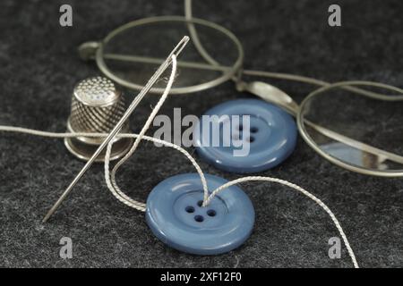 Nahaufnahme aus grauem Stoff, bereit zum Schneiden mit Schere, Garn, Nadel-Fingerhut und Knöpfen Stockfoto