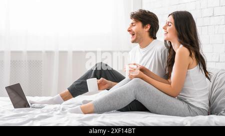 Glückliches Paar, Das Sich Im Bett Mit Laptop Und Kaffee Entspannt Stockfoto