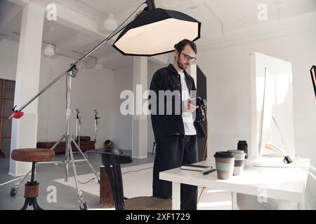 Weitwinkelansicht eines professionellen Fotografen, der die Kamera für Fotoaufnahmen im weißen Studio mit großer Kranbeleuchtung und Kopierraum hält Stockfoto