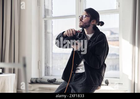 Minimales Porträt eines männlichen Fotografen, der am Fenster steht und die Kamera hält, während er während des Fotoshootings Anweisungen zum Modell gibt, Kopierraum Stockfoto