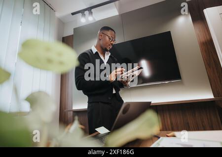 Professioneller afroamerikanischer Geschäftsmann, der Dokumente in moderner Büroumgebung überprüft Stockfoto