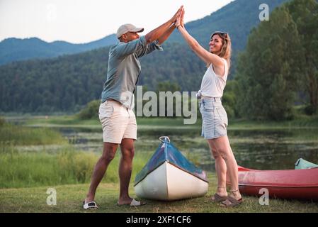 Glückliches junges Paar bei einer Kanufahrt, die High 5 auf einem wunderschönen grünen See gibt Stockfoto