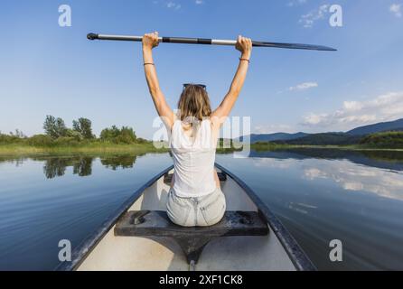 Frau genießt eine erstaunliche Sommer-Naturszene beim Kanufahren im See, Rückansicht. Kanu-Abenteuer und entspannende Konzepte. Stockfoto
