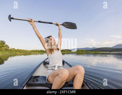 Aktive junge Frau paddelt mit einem Kanu auf einem See umgeben von grüner Sommernatur, Nahaufnahme. Kanu-, Therapie- und Erholungskonzepte. Stockfoto