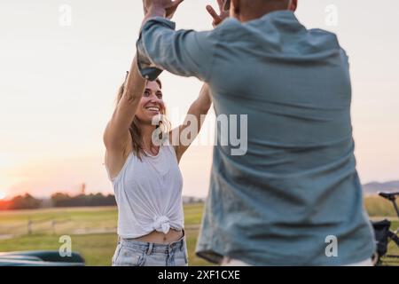 Glückliches junges Paar bei einer Kanufahrt, die High 5 auf einem wunderschönen grünen See gibt Stockfoto