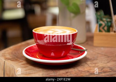 Nahaufnahme einer roten Espresso-Tasse mit Milchschaumkunst auf einem Retro-Holztisch in einem Café Stockfoto