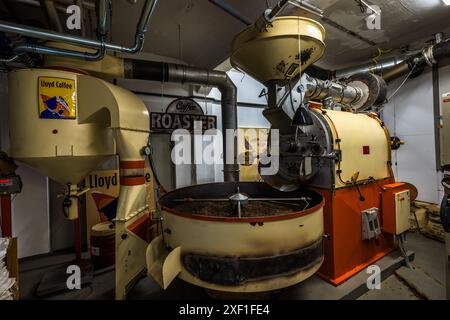 Die Trommelröstmaschine von Lloyd Caffee steht in einem rohrverlegten Kellergeschoss im Überseehafen von Bremen. Ein Schild mit der Aufschrift „Kaffeerösterei“ markiert die historische Ausrüstung, bei der die Kaffeeseminare von Lloyd Caffee mit Röstung und Verkostung enden. Hagstraße, Bremen, Deutschland. Stockfoto
