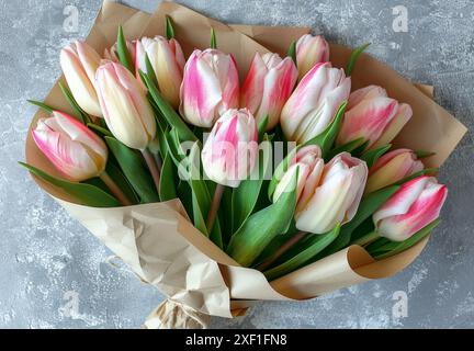 Strauß aus rosa und weißen Tulpen, in braunes Papier gewickelt. Die Tulpen sind in klassischer Straußform angeordnet, wobei die Stiele fest miteinander verbunden sind. Th Stockfoto