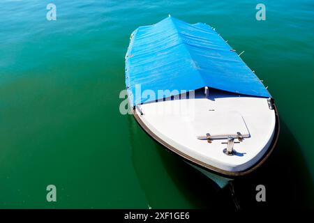 Das Boot mit einer blauen Plane auf der Oberseite sitzt im Wasser. Das Boot ist klein und hat ein weißes Oberteil Stockfoto