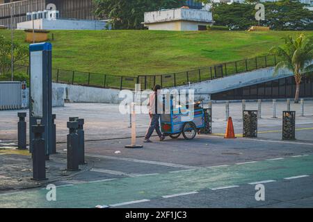 Jakarta, Indonesien - 11. Mai 2024. Ein junger indonesischer Mann, voller Energie, schiebt seinen blau gefärbten Lebensmittelkarren eine Stadtstraße hinunter. Er ist eifrig, anzufangen Stockfoto