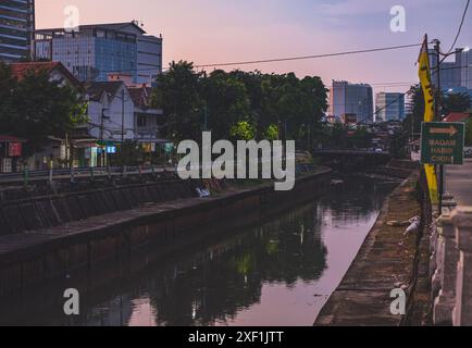 Jakarta, Indonesien - 10. Mai 2024. Eine malerische Landschaft des Flusses Ciliwung mit farbenfrohen Gebäuden am Ufer, beleuchtet durch das warme Licht der Dämmerung. Stockfoto