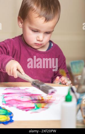 Kleinkinder experimentieren mit Aquarellen und einem großen Pinsel auf einem leeren Stück Papier. Stockfoto