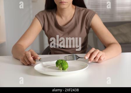 Essstörung. Frau hält Besteck in der Nähe von Brokkoli an einem weißen Tisch drinnen, Nahaufnahme Stockfoto