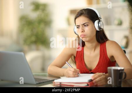 Frustrierter Schüler mit Kopfhörern, der zu Hause Online-Unterricht anhört Stockfoto