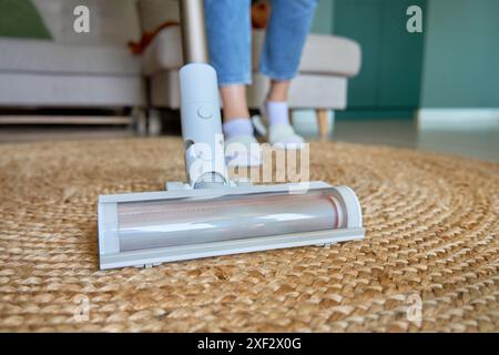 Nahaufnahme der Staubsaugerbürste, die den Teppich auf dem Boden reinigt. Frau mit tragbarem schnurlosem Staubsauger. Tägliche Routine und Hausaufgaben Stockfoto