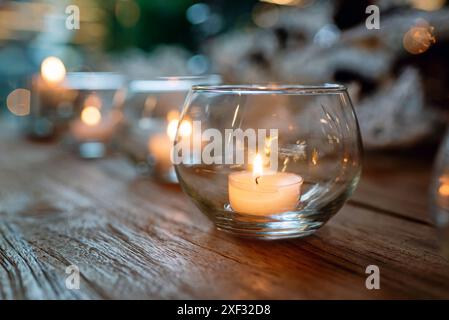 Reihe von Glasschalen mit brennenden Kerzen auf Holztisch vor verschwommenem Hintergrund Stockfoto