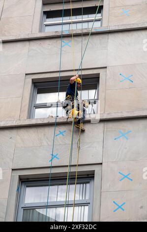 Ein Techniker für den Seilzugang verwendet einen Bohrer, während er an Seilen hängt Stockfoto