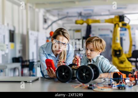 Eine Lehrerin hilft jungen Schülern beim Bau eines Roboterautos im Robotikclub. Kinder, die Robotik in der Grundschule lernen. Wissenschaft Stockfoto