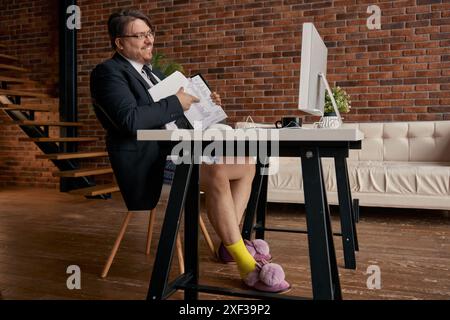 Lustiger Geschäftsmann mit formellem Anzug und weichen Hausschuhen, der online arbeitet Stockfoto