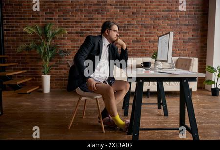 Lustiger Geschäftsmann im formellen Anzug und weiche Hausschuhe, der online arbeitet Stockfoto