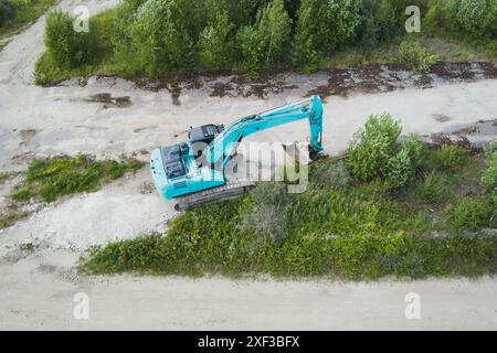 Ein blauer Bagger steht in einem offenen Bereich, Fotoaufnahme von einer Drohne. Stockfoto