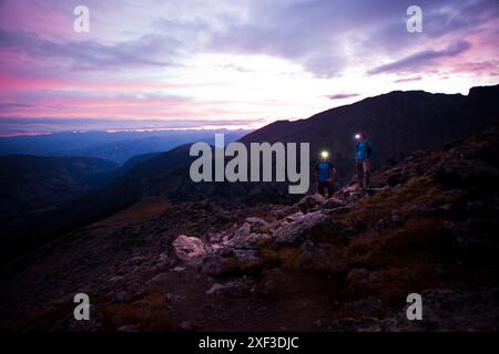 Eine Frau und ein Mann mit Scheinwerfern halten kurz vor Sonnenaufgang auf einem alpinen Talusfeld in Colorado für eine Pause an. Stockfoto