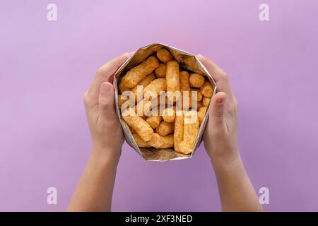 Kinderhände, die ein Paket Bamba offen halten. Bamba ist ein beliebter Snack in Israel. Es besteht aus Papageienkörnern mit Erdnussbutter-Geschmack. Nahaufnahme Stockfoto