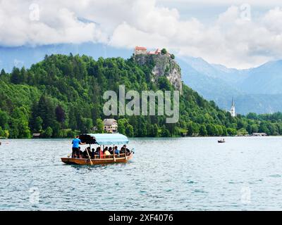 Traditionelles Holzboot oder Pletna, das die Insel Bled mit der Burg Bled hinter der Oberen Karniola von Bled in Slowenien verlässt Stockfoto