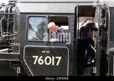 Nahaufnahme des Fahrers und Feuerwehrmanns auf der Fußplatte des Wealden Pullman, Lokomotive Nr. 76017, rückwärts zum Zug, am Bahnhof Tenterden, Stockfoto