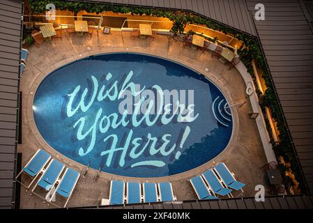 Ein ruhiger Hotelpool in Honolulu, mit den Worten "Wish you were here" unten geschrieben. Das kristallklare Wasser reflektiert die tropische Umgebung Stockfoto