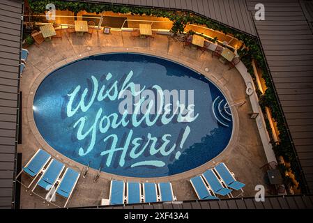 Ein ruhiger Hotelpool in Honolulu, mit den Worten "Wish you were here" unten geschrieben. Das kristallklare Wasser reflektiert die tropische Umgebung Stockfoto