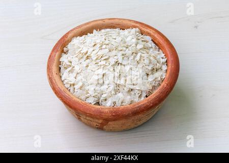 Chira oder flacher Reis auf einem Erdtopf auf hölzernem Hintergrund. Es ist auch bekannt als poha, pohe, aval, Pauwa, sira, Chivda, Chiwda oder Avalakki. Stockfoto