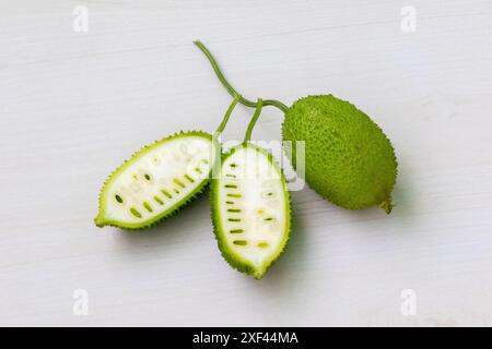 Geschnittenes und ganzer stacheliges Kürbis-grünes Gemüse auf hellem weißem hölzernem Hintergrund. Momordica dioica ist auch bekannt als Kakrol, Kartoli, Kankoda, Kantola. Stockfoto