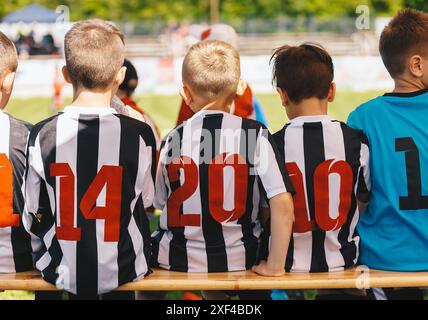 Fußballspiel für Schulkinder. Kinder in Sportmannschaften, die von einem jungen Trainer trainiert werden. Kinder sitzen während der Halbzeitpause auf einer Holzbank. Socc Stockfoto