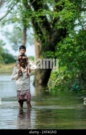 Ein Vater, der seinen Sohn auf den Schultern trägt, watet durch die Fluten im Gebiet Shalutikor bei Guainghat upozila von Sylhet. Bangladesch. Stockfoto